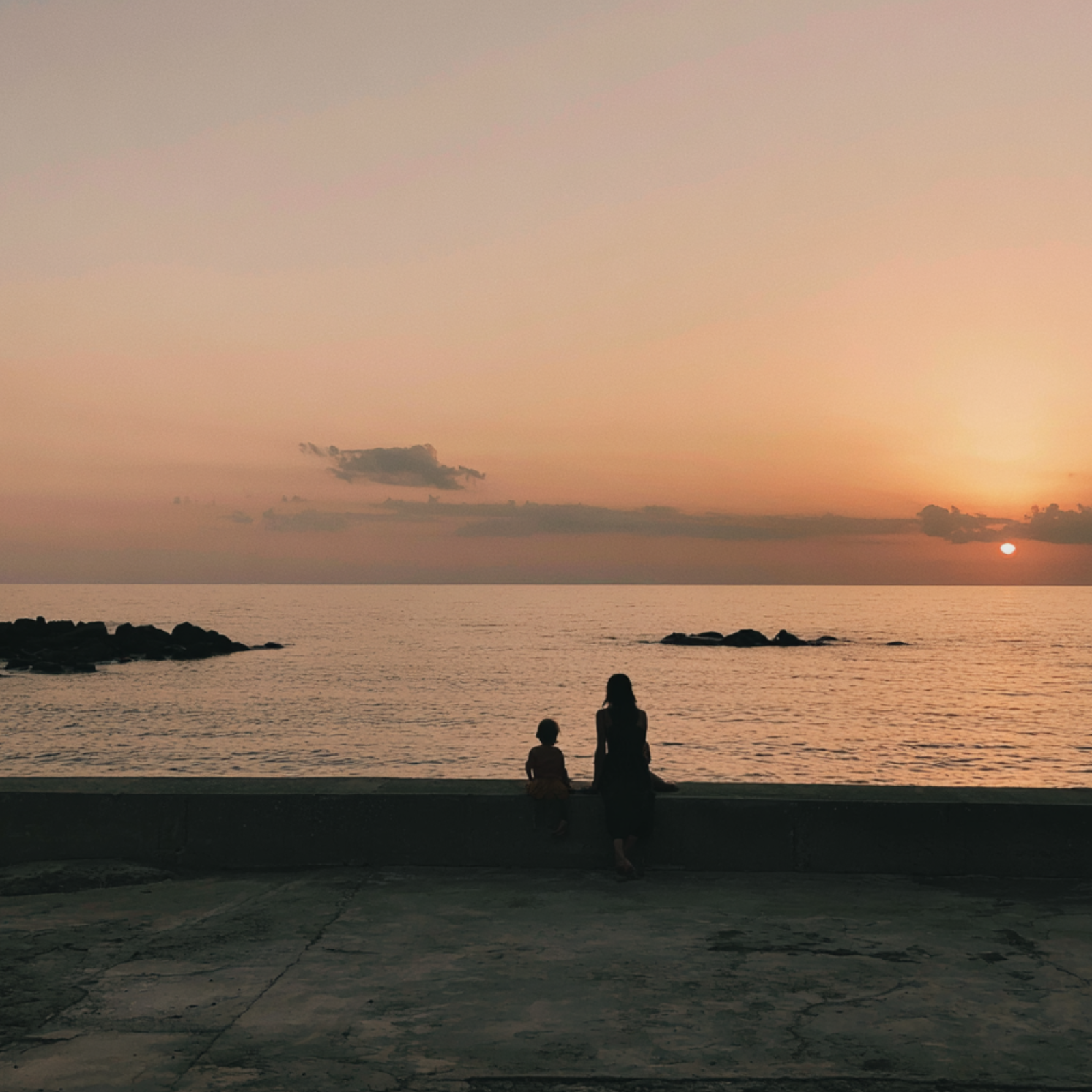 Una donna e un bambino guardano il tramonto mentre si trovano a pochi passi dal mare